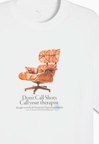 Hvid t-shirt med en illustration af en brun læderstol med en træbase, ledsaget af trykt tekst under billedet.