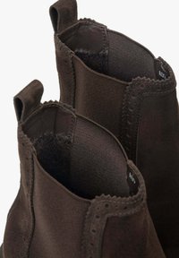 Brązowe zamszowe botki za kostkę z elastycznymi bokami, teksturowanym materiałem i dekoracyjnym przeszyciem wokół otwarcia. Posiadają design typu slip-on.