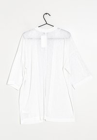 Lekka biała bluzka w stylu kimona z rękawami o długości trzy czwarte, prześwitująca tkanina i luźny krój. Zawieszona na czarnym haczyku do ekspozycji.
