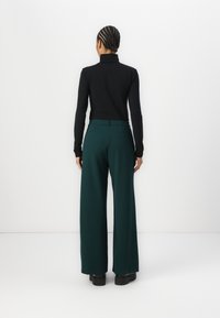 Zwarte coltrui gecombineerd met hoge taille, wijde groene broek. De broek heeft achterzakken en een soepele stoftextuur.