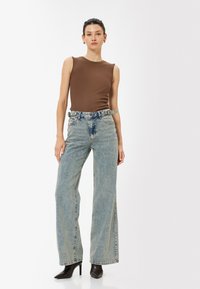 Brun ribbad ärmlös topp i kombination med högmidjade, vida ljusblå jeans. Svarta pumps med spetsig tå fulländar outfiten.