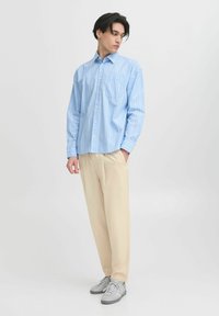 Langermet, lyseblå stripete skjorte med krage som knappes, kombinert med beige bukser og grå sneakers. Slim fit, myk stoff.