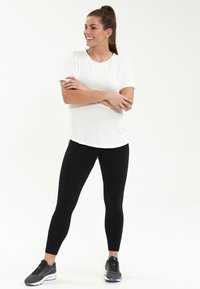Vit t-shirt med kort ärm och rund halsringning, ihopparad med svarta leggings och grå sportskor med blå accenter.