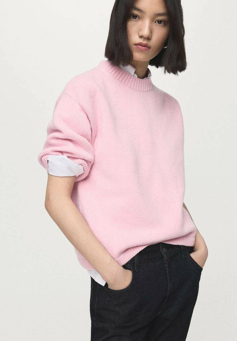 Light pink sweater with a textured finish, rolled sleeves, and a ribbed neckline, paired with dark jeans. Simple design, soft fabric.
