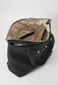 Zwarte geweven strandtas met dubbele handvatten, accenten van goudkleurig beslag en een beige interieur met een herhaald logo-patroon. Met ritssluiting.