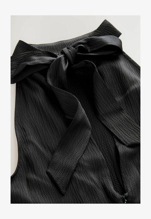 Črna bluza iz teksturiranega materiala, z izrazitim metuljčkom na izrezu in zadrgo spredaj. Material je lahek in guban.