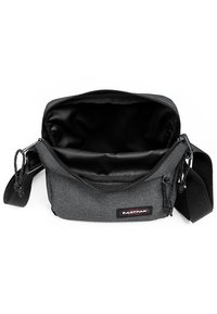 Borsa a spalla in tessuto grigio con chiusura a zip, tracolla regolabile e interno nero liscio. Presenta un piccolo patch con logo sulla parte anteriore.