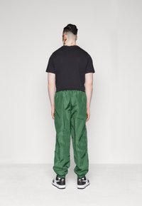 Träningsoutfit med en svart T-shirt och blanka gröna träningsbyxor med elastisk midja, kombinerad med svarta och vita sneakers.