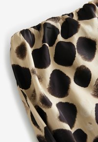 Tissu satin présentant un motif abstrait de taches dans des tons de noir et de beige. Le tissu a une texture lisse avec des bords froncés.