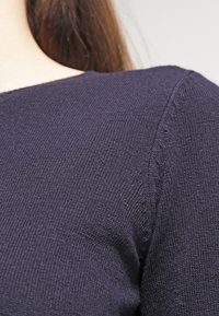 Mörkblå stickad tröja med en strukturerad tyg, som har en klassisk rund halsringning och subtila sömdetaljer på axlarna.