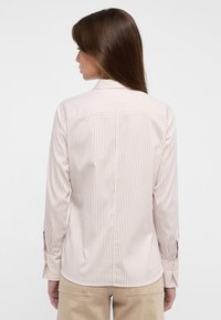 Gestreiftes Shirt aus weichem Material, hellbeige mit dunkleren Streifen, taillierte Passform, lange Ärmel mit Knopfmanschetten und abgerundetem Saum.