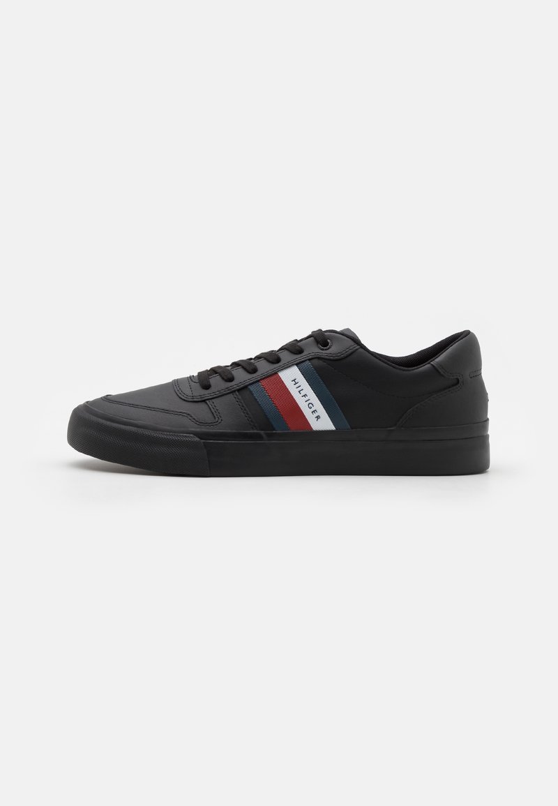 Sneaker nera con tomaia sintetica liscia, caratterizzata da strisce orizzontali rosse e blu, suola in gomma testurizzata e design con lacci.