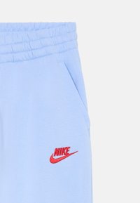 Gaiši zili treniņbikses ar elastīgu jostasvītru un sānu kabatām, ar sarkano Nike logo izšūtu uz apakšējās kājas.