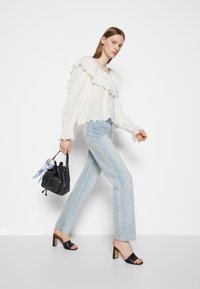 Weiße, geraffte Bluse mit Lochstickerei, hellblaue weite Jeans, schwarze Peeptoe-Blockabsätze und eine kleine schwarze Bucket Bag.