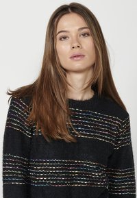 Fekete pulóver színes vízszintes csíkokkal, különböző kötési mintákkal, kerek nyakkal és puha tapintással; laza fazon.