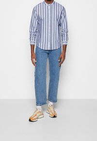 Randig blå och vit skjorta med knäppning och krage, parat med ljusblå denimjeans och sneakers med orange accenter.