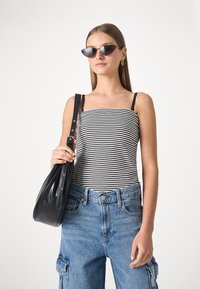 Pruhované černobílé tílko, modré džíny typu cargo a černá kabelka přes rameno. Modelka nosí tmavé sluneční brýle a má dlouhé vlasy.