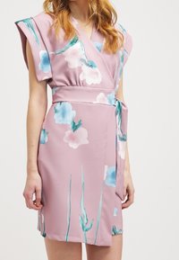 Robe portefeuille rose à fleurs avec de courtes manches cape, présentant des fleurs bleues et blanches semblables à de l'aquarelle, une ceinture à la taille et une texture de tissu lisse.