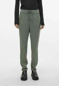 Lichtgroene sweatpants met een trekkoord in de taille, twee zijzakken en een taps toelopende pasvorm, gecombineerd met zwarte instappers. Glad textuur van de stof.