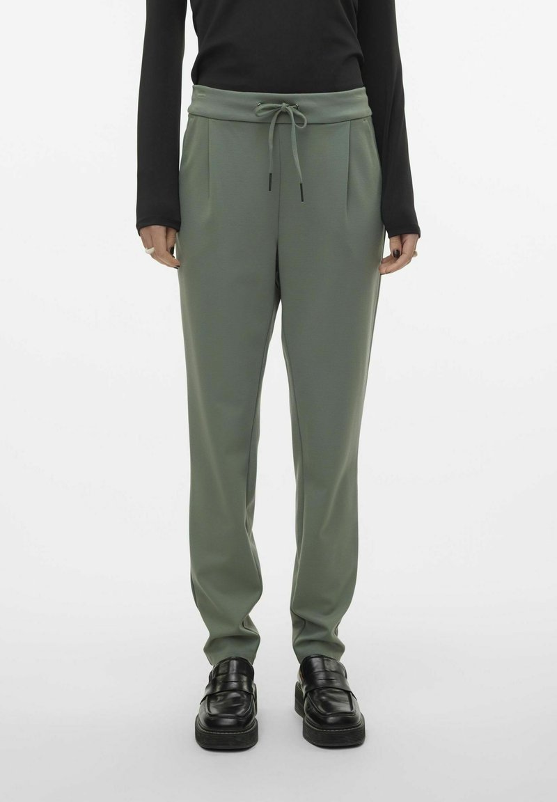 Lichtgroene sweatpants met een trekkoord in de taille, twee zijzakken en een taps toelopende pasvorm, gecombineerd met zwarte instappers. Glad textuur van de stof.
