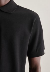 Polo nero realizzato in tessuto testurizzato, con colletto classico e maniche corte. Stile liscio e aderente con dettagli minimi.