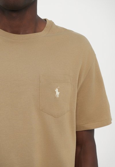 T-shirt beige à manches courtes en coton, doté d'une poche poitrine et d'un logo brodé blanc d'un cheval et d'un cavalier sur la poche.