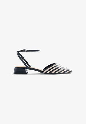 Zapato plano de punta con rayas blancas y negras, con correa en el tobillo y tacón bajo en bloque sobre fondo blanco.