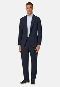 Granatowy garnitur o dopasowanym kroju, z jednoozdobnym marynarką i pasującymi spodniami. Noszony z jasnoniebieską koszulą w paski i czarnymi trampkami.