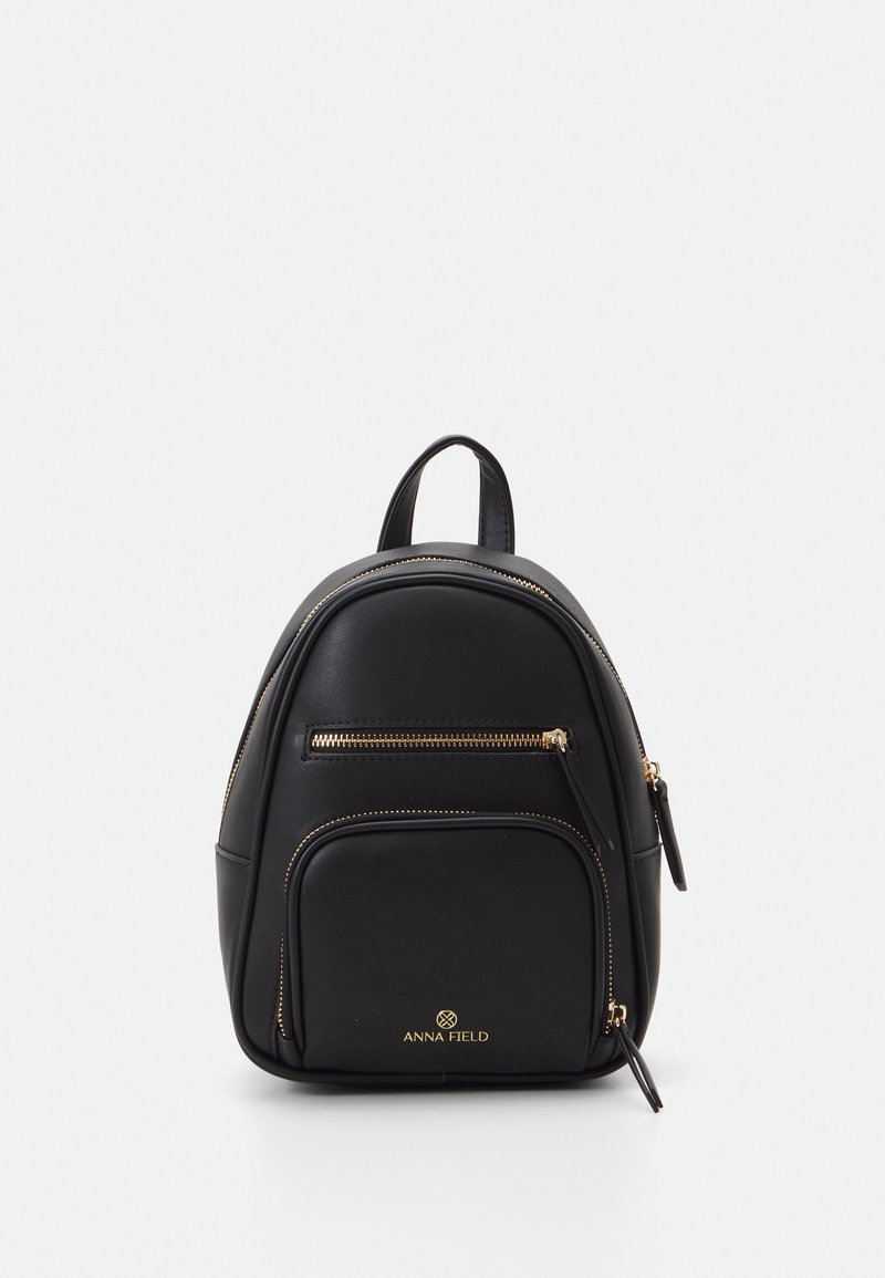 Mini-sac à dos noir avec deux poches zippées dorées et une anse supérieure, avec le logo "ANNA FIELD" en doré sur la poche avant.