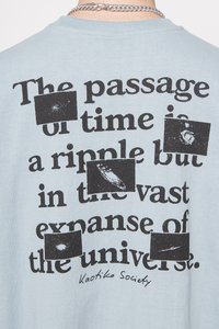 Light blue cotton t-shirt featuring black text. Graphic details include several black squares with distressed designs overlapping the text.
