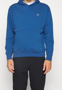 Sudadera azul hecha de un tejido suave, con un bolsillo canguro en la parte delantera, puños acanalados y un pequeño logo blanco en el pecho.