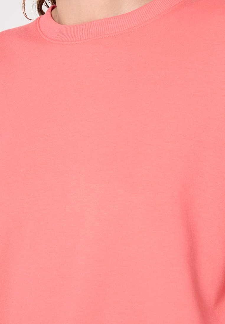Korallenfarbene Sweatshirt mit geripptem Rundhalsausschnitt und weicher, glatter Textur; der Stoff ist leicht und lässig ohne sichtbare Muster.