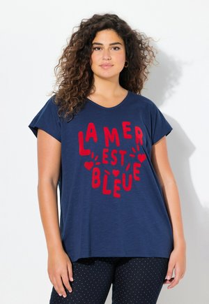 T-shirt bleu marine à manches courtes avec un texte rouge indiquant "LA MER EST BLEUE." Tissu doux, coupe décontractée, col rond, associé à des leggings à pois.