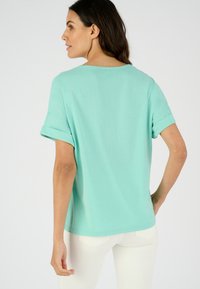 Top de color verde menta de manga corta con puños enrollados, que presenta un ajuste relajado y una tela suave y ligera. Vista trasera destacada.