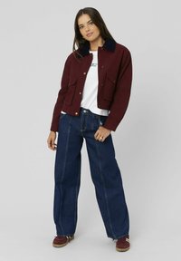 Veste courte bourgogne avec un col en velours côtelé bleu marine, deux poches avant ; associée à un jean large bleu foncé et des baskets bordeaux.