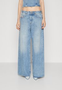 Jeans en denim bleu clair à jambes larges, avec une taille haute, cinq poches et une finition décolorée. L'ourlet est légèrement effiloché.