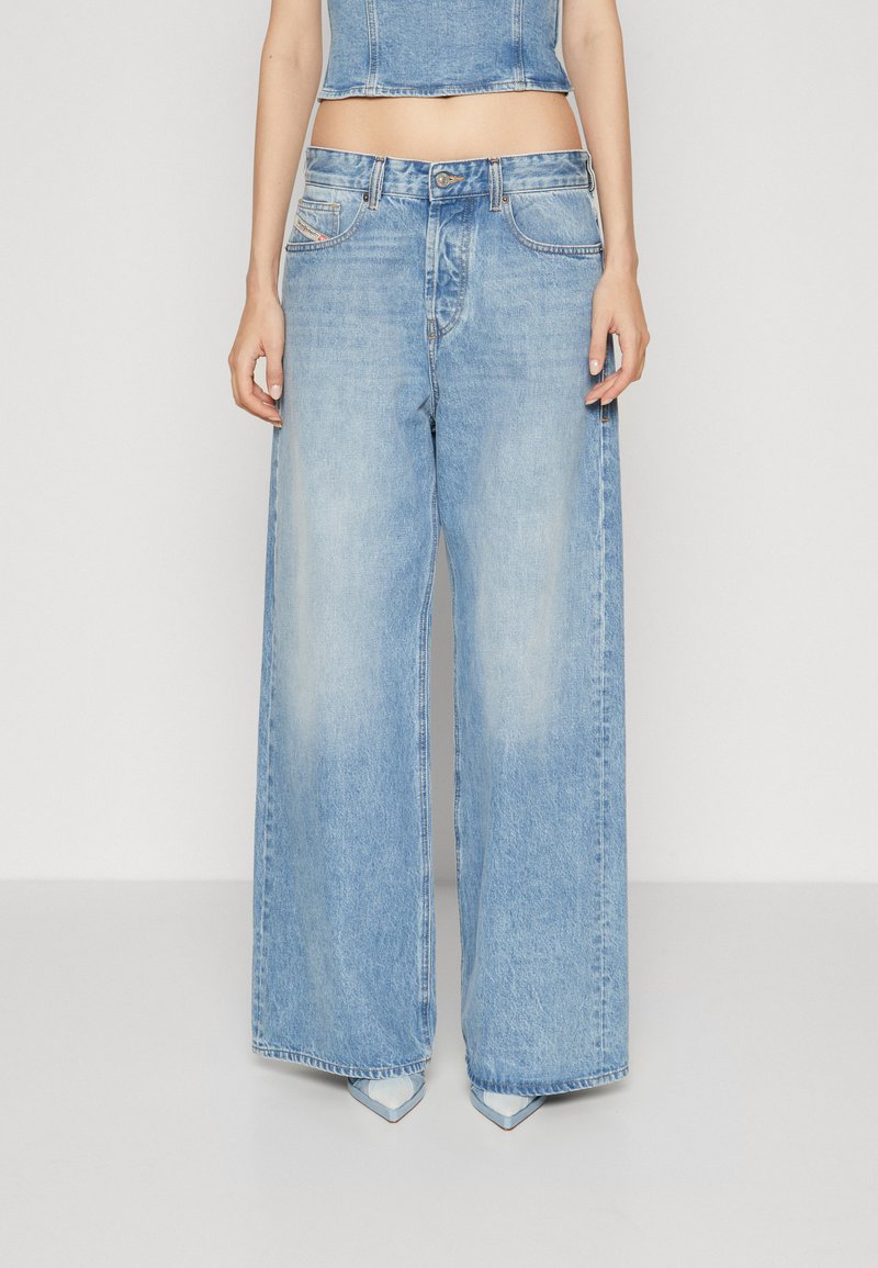 Jeans en denim bleu clair à jambes larges, avec une taille haute, cinq poches et une finition décolorée. L'ourlet est légèrement effiloché.