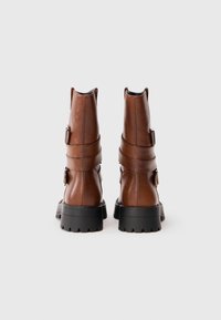 Pruunide nahast ankle boots, millel on kaks rihma ja pistikut, tekstureeritud pind ja jäme must kummist tald.