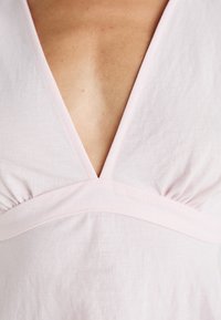 Lichtroze jurk met een diepe V-halslijn en geplooide details onder de buste, gemaakt van zachte, lichte stof.