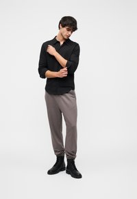 Μαύρο πουκάμισο με κουμπιά, γκρι φόρμα, και μαύρα μποτάκια με κορδόνια. Το πουκάμισο έχει μακριά μανίκια, ενώ το παντελόνι διαθέτει άνετη εφαρμογή και ελαστικά τελειώματα.