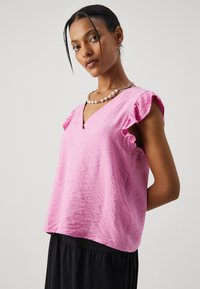 Top leggero rosa con scollo a V e maniche a volant. Il tessuto ha una finitura testurizzata, che si abbina a una gonna nera fluttuante.