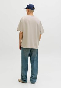 T-shirt beige oversize, manches courtes, encolure ronde, associé à un jean bleu clair ample et une casquette de baseball bleu marine.