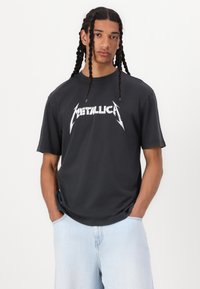 T-shirt en coton noir avec un grand logo "Metallica" blanc agrémenté d'éclairs. Manches courtes et coupe décontractée.