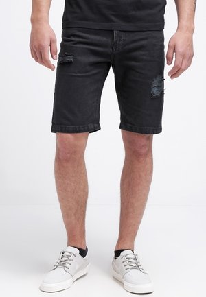 Black denim shorts with distressed tears, regular fit, and a cuffed hem. Paired with light gray sneakers on a plain background.