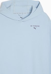 Ανοιχτό μπλε φούτερ με κουκούλα, με εκτύπωση "HYROX" και λογότυπο Puma σε μαύρο στο στήθος, και επαναλαμβανόμενο λογότυπο στην ταινία στον λαιμό μέσα στην κουκούλα.