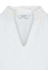 Encolure de blouse blanche avec col à volants et profond décolleté en V, avec une étiquette "b.young THE COLLECTION" au dos.