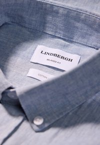 Camicia in cotone azzurro chiaro con una vestibilità rilassata. Presenta un colletto button-down, un tessuto testurizzato e un'etichetta che mostra il marchio e le informazioni per la cura.