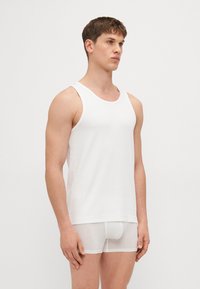 White tank top made of smooth cotton fabric, featuring a round neckline and sleeveless design, paired with sheer white briefs.