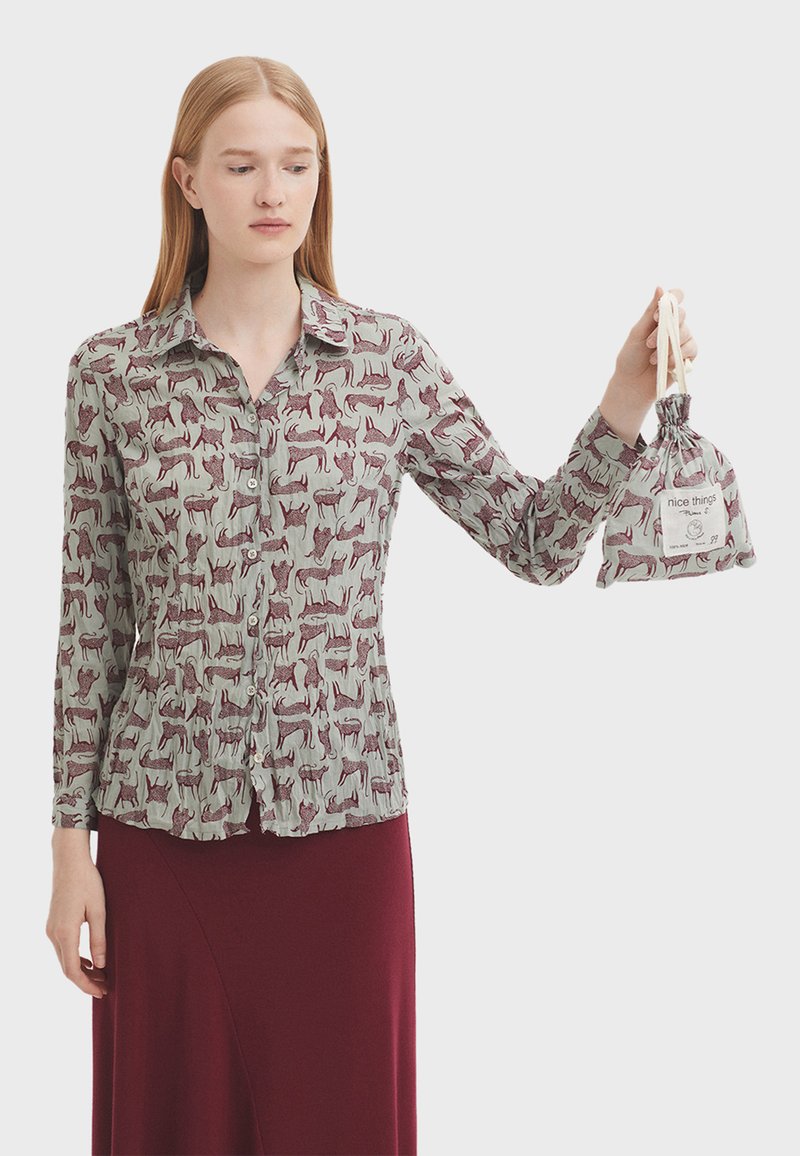 Camicia a maniche lunghe con sfondo verde chiaro e stampa animale bordeaux, abbinata a una gonna bordeaux scura. Presenta bottoni frontali e una borsa coordinata.