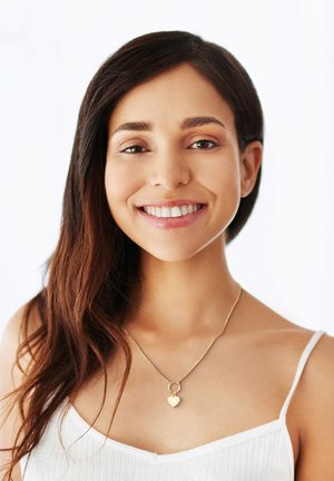 Goldener Herzanhänger mit einer feinen Kette, der einen strukturierten Herzcharme und einen kreisförmigen Schlaufenakzent zeigt, getragen über einem weißen Rippentop.